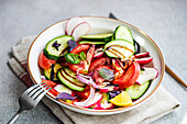 Hochformatiger, schmackhafter vegetarischer Salat mit Gurke, Zitrone, Zwiebel und Tomate mit grünen Blättern und Dressing in einer Schale auf dem Tisch