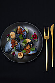 Fresh mussels and scallops on a black plate