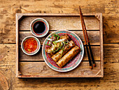 Spring rolls with sauce in a wooden tray on a wooden base