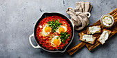 Frühstück Shakshuka Spiegeleier mit Tomaten in der Pfanne und Brot mit weichem Ziegenkäse auf Betonhintergrund copy space