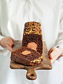 Travel Cake or Tube Cake or Voyage Cake, filled with ganache in the centre and topped with chocolate icing and pistachios (can also be made with peanuts). Chocolate cake with chocolate cream cheese filling in the centre. Idea and recipe for baking with ganache cream centre. Loaf cakes on women's hands