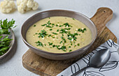 Cream of white vegetable soup. The dish is flavoured with parsley and garlic. There is a spoon and a napkin nearby