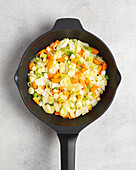 Top view of a fumet-filled roasting pan with carrots, cabbage and green string on a grey kitchen table