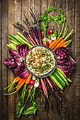 Overhead shot of onion dip in a bowl surrounded by fresh, colorful vegetables on a wood background