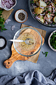 Salatdressing mit Zitronensaft und Olivenöl in einer kleinen Glasschale auf einem Holzbrett und Thunfisch-Kartoffelsalat an der Seite