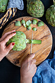 Woman's hand cutting the stem of an artichoke on a round wooden board
