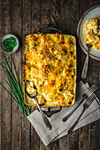Cauliflower cheese in a baking dish on wood table with chives and serving on plate