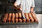 Baker spreads sugar syrup icing on a tray of fruit buns made from yeast and sourdough