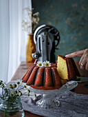 Sliced citrus cake, decorated with flowers, on a glass stand next to the window