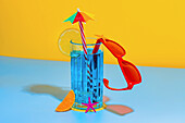 Composition of glass with blue liquid, lemon slice and straw with stylish red glasses on a light blue and yellow background in the studio