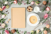 White cup of coffee, empty notebook and Frame made of Spring flowers and different types of macaroons flat lay mock up copy space
