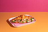 Leckeres Croissant mit Schinken, Käse und Rucola auf einem Teller mit buntem Hintergrund von oben