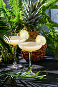 Sommercocktail Ananas-Daiquiri mit Wodka, Ananassaft, gefrorener Bewegung und fliegenden Tropfen. Tropischer Hintergrund mit Palmenblättern