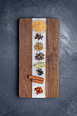 Coriander seeds, cloves, mustard seeds, black peppercorn, bay leaves, cloves, cinnamon sticks, red pepper flakes photographed on a wooden cutting board.