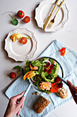 Frauenhände servieren mediterranen Salat mit Zucchini, Kapuzinerkresse und essbaren Rosenblüten, Flatlay