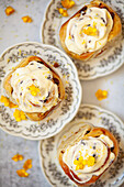 Three lemon rolls topped with cream cheese frosting, presented on plates and garnished with yellow flowers.