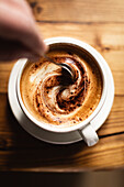 Person stirring coffee in a white cup on a wooden table