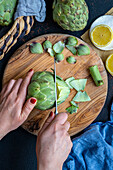 Women's hands cut off the tip of an artichoke on a wooden board