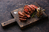 Sliced grilled beef steak and pepper mill on wooden board
