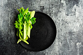 Celery sticks from above on a black plate on a grey concrete surface