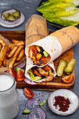 Chicken doner wraps served with chips, pickles and salad on a wooden board.