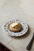 Crumpet with butter on blue floral plate on a marble table.