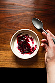 Bowl of yoghurt and blackberry compote on an antique wooden table with a silver spoon