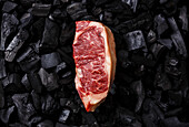 Rohes Frischfleisch Striploin-Steak auf schwarzem Holzkohle-Hintergrund