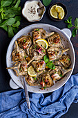 Roasted artichokes in a round baking tin, garnished with mint and lemon