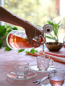 Pouring orange tea in glass teacups against a pink background
