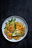 Salad with avocado, mandarins, oranges, rocket and various seeds on a dark background. View from above