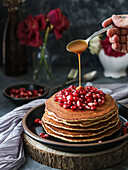 Stack of pancakes with pomegranate, red flowers and caramel on a black plate and a dark background