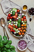 Flatlay of a Greek salad with fresh basil and spoons on a light backdrop