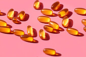 Composition of orange vitamin pills scattered on pink background in light studio
