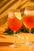 Aperol Spritz Cocktail mit Eis, ein beschlagenes erfrischendes Getränk, auf einem orangefarbenen Hintergrund, Sonnenlicht, Schatten, ein Sommergetränk in einem Weinglas