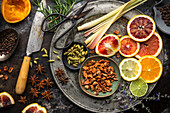 Flat lay arrangement of colourful citrus slices, fruit juices, lemongrass, herbs and spices on a dark background. Ingredients for homemade tonic water for cocktails