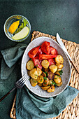 Roasted spring potato with fresh dill herb and raw vegetable salad served in the bowl near water with lemon