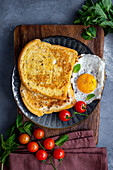 A breakfast plate loaded with French toast slices and a fried egg garnished with fresh mint leaves and cherry tomatoes.