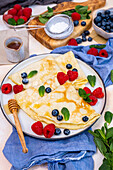 Almond milk crepes garnished with fresh berries and mint leaves on a round plate.