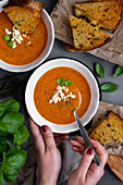 Eine Frau hält eine Schüssel Tomatensuppe und den Löffel darin, eine weitere Schüssel Tomatensuppe und gegrillte Käsesandwiches an der Seite
