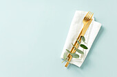Gold Cutlery with eucalyptus branches on white linen napkin over blue Background. Minimalistic design. Copy Space