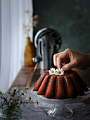 Citrus cake decorated with flowers on a glass stand next to the window