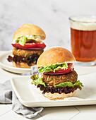 Two vegan burgers on white plates with beer