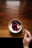 Bowl of yoghurt and blackberry compote on antique wooden table with silver spoon