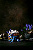 Homemade traditional Easter panettone cake with blue ribbon, colored black eggs in moss, blossoming muscari flowers on black wooden table. Traditional Easter Italian bake, copy space