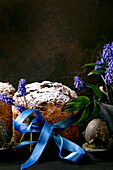 Hausgemachter traditioneller Oster-Panettone-Kuchen mit gefärbten schwarzen Eiern, blühenden Muscari-Blumen auf schwarzem Holztisch. Traditionelle italienische Osterbäckerei, Kopierraum, Nahaufnahme