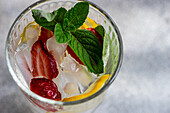 Draufsicht auf ein Sommercocktailglas mit Eis, Minze, Zitrone und Erdbeere im Glas vor unscharfem Hintergrund