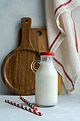 Raw cow milk in vintage closed bottle near drinking straws on gray surface against blurred napkin and cutting board