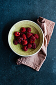 From above of bowl with ripe raspberries and placed on a dark concrete table