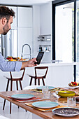 Side view of crop Male cook taking photo on smartphone of served table for breakfast in modern dining room during work